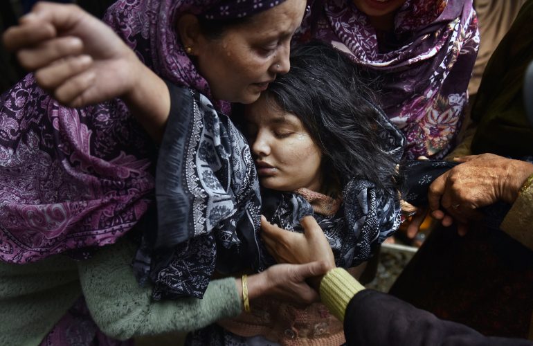 A grieving woman holds a young girl in her arms, surrounded by others offering support and comfort.
