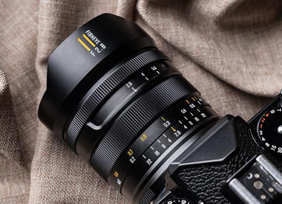 Close-up of a fisheye camera lens attached to a black camera, resting on a textured brown fabric.