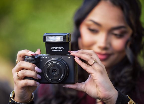 A woman holding a Sony camera with a flash, focusing as she prepares to take a photo outdoors.
