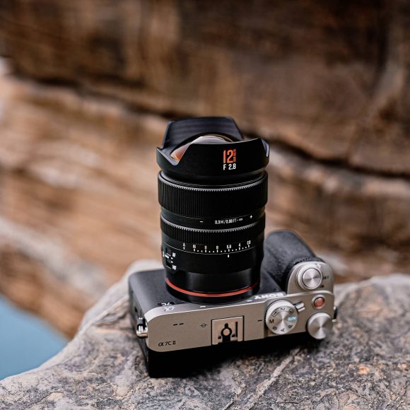 A mirrorless camera with a large lens sits on a rocky surface near a blurred cliff edge.