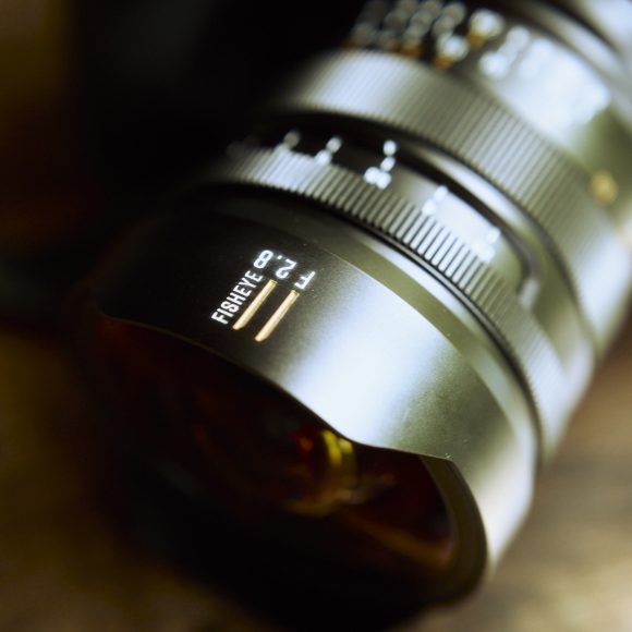 Close-up of a fisheye camera lens on a wooden surface, with a red circular logo in the corner.
