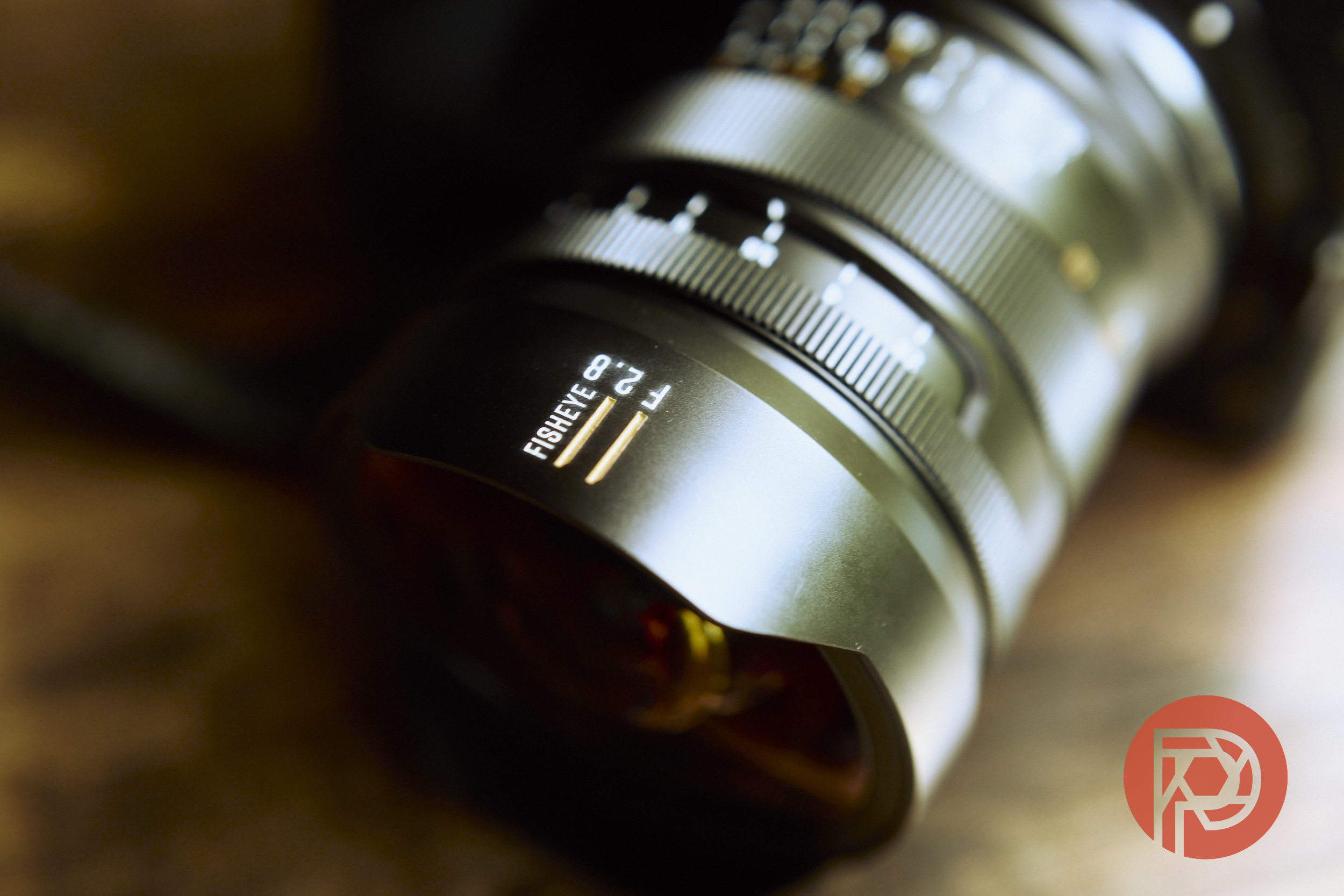 Close-up of a fisheye camera lens on a wooden surface, with a red circular logo in the corner.