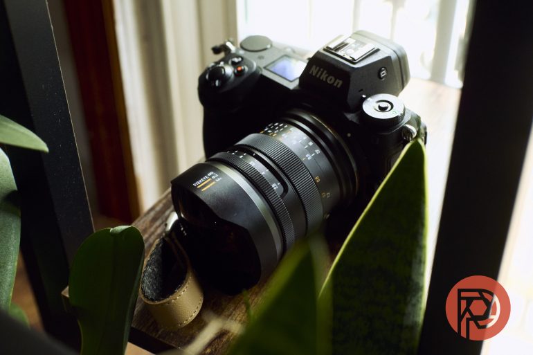 Nikon camera with lens placed on a wooden surface near green plants and a window, with soft natural light.
