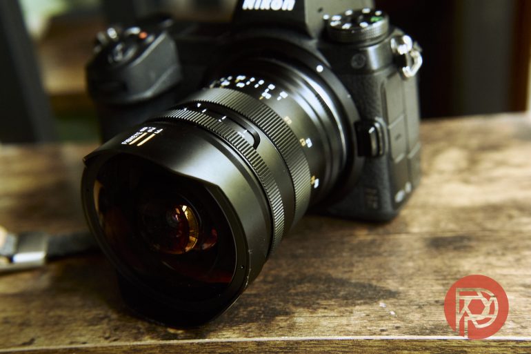 A Nikon camera with a wide-angle lens rests on a wooden surface.