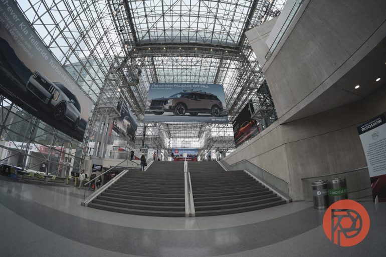 A spacious, modern convention center lobby with wide stairs and large car advertisements.