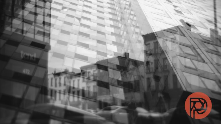 Abstract reflection of buildings in a glass facade, with a red circular logo at the bottom right corner.