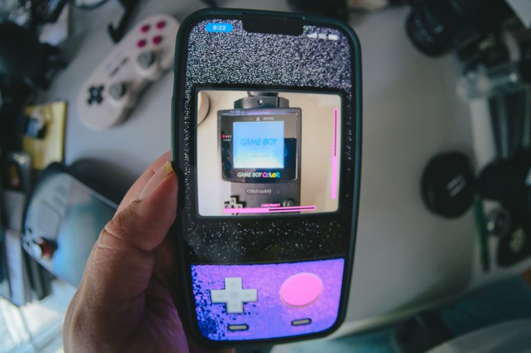 A hand holds a phone with a Game Boy-themed case, displaying a Game Boy Color screen.