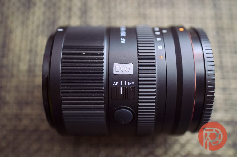 Close-up of a black camera lens showing focus and mode switches, placed on a textured surface.