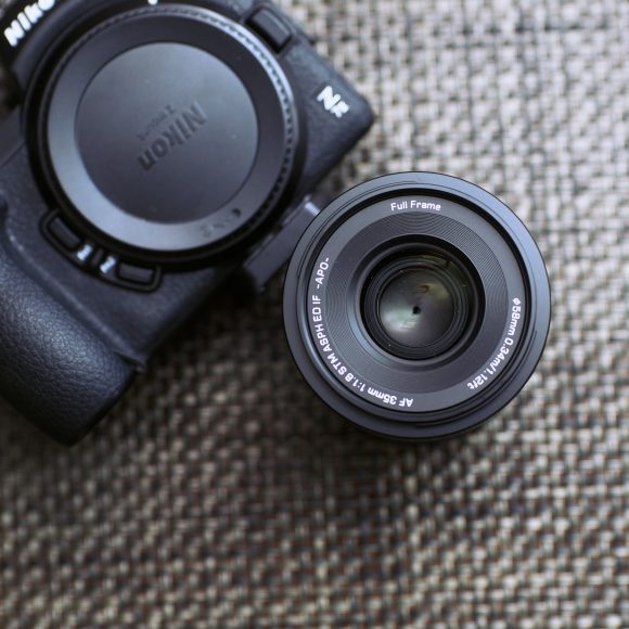 A Nikon camera with a detached 50mm lens on a textured surface, with a red logo in the corner.