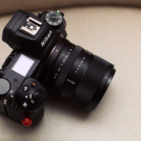 A Nikon camera with a Viltrox 24mm lens rests on a beige surface, with a red logo in the corner.