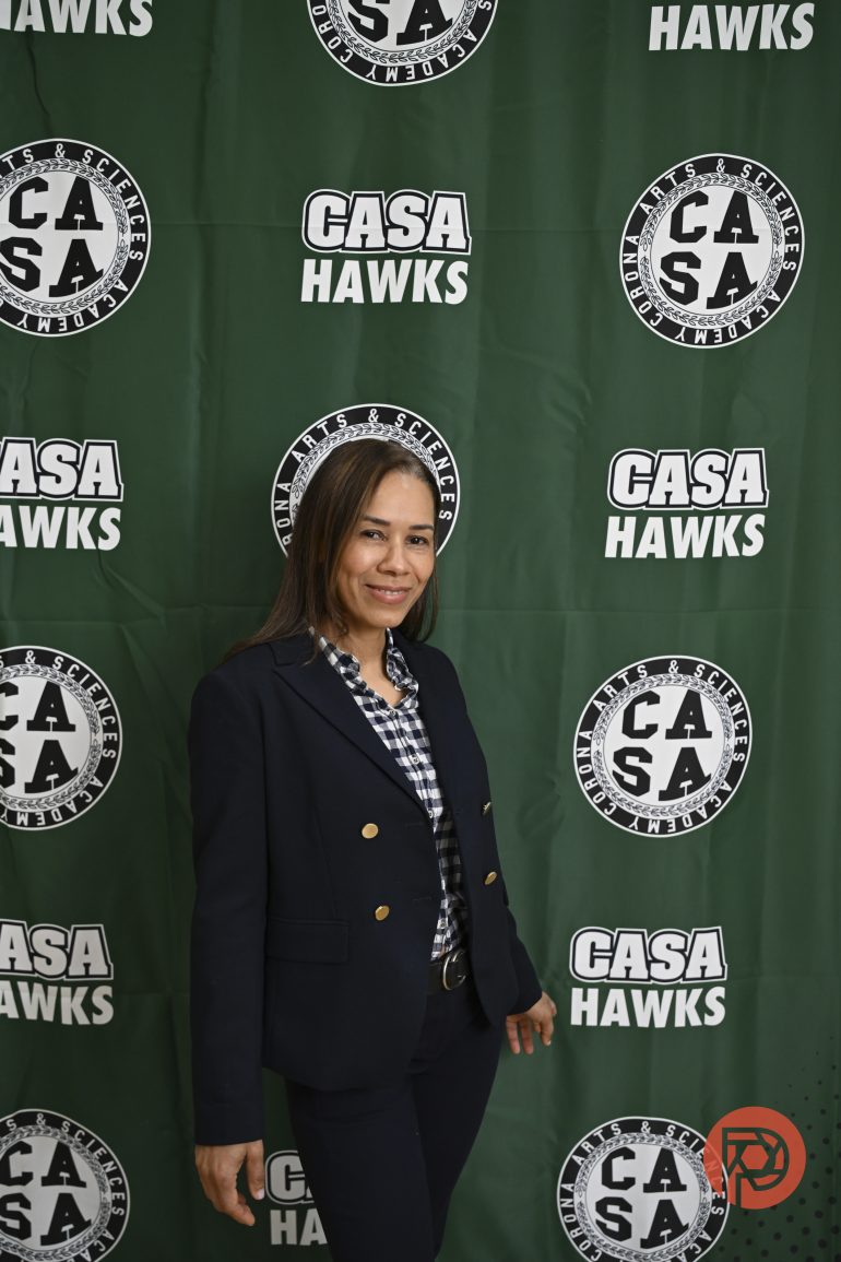 A woman in a navy suit stands in front of a green CASA Hawks step-and-repeat banner.