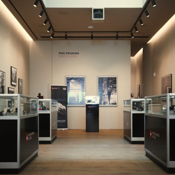 A modern gallery with glass display cases, framed photos on the walls, and wooden floors.