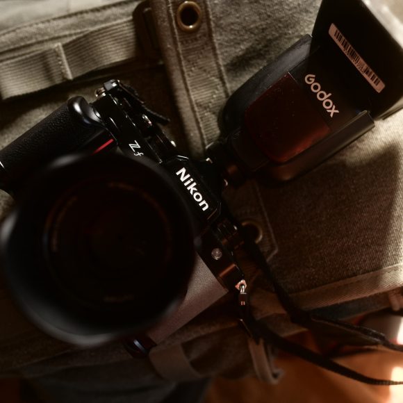 A Nikon Z7 camera with a Godox flash rests on a padded gray camera bag.