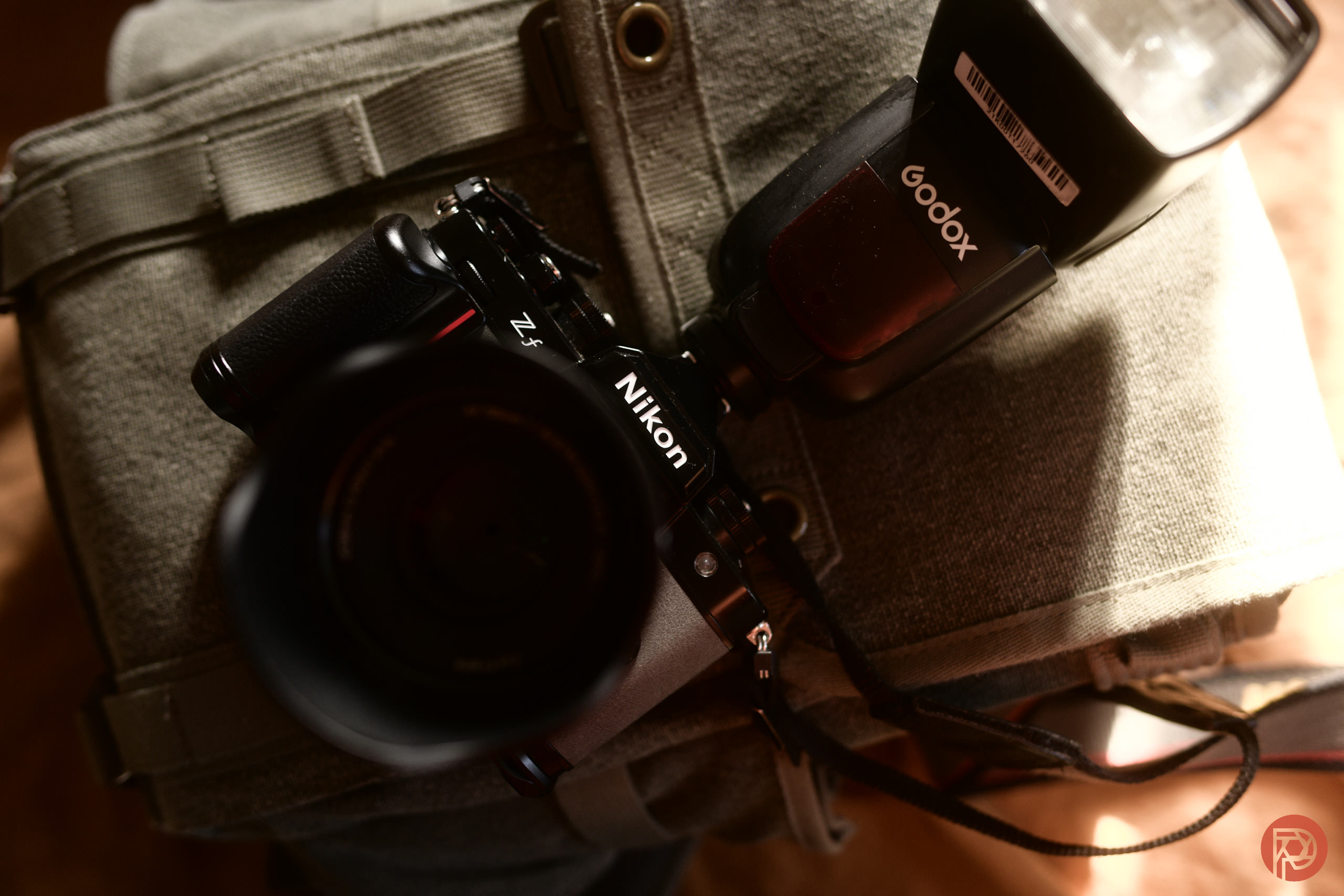 A Nikon Z7 camera with a Godox flash rests on a padded gray camera bag.