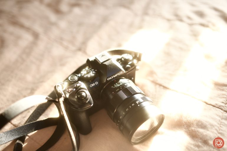 A black Olympus camera with a lens and strap resting on a sunlit, beige surface.