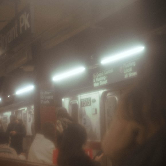 Soft-focus photo of people waiting for a subway train at Bryant Park station in New York City.