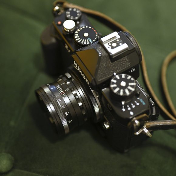 A vintage Nikon film camera with a lens and strap rests on a dark green fabric surface.