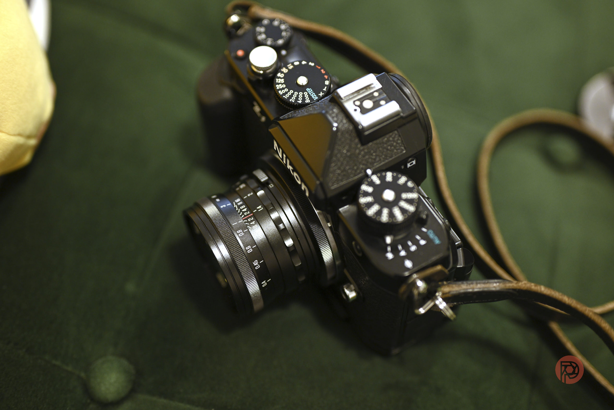 A vintage Nikon film camera with a lens and strap rests on a dark green fabric surface.