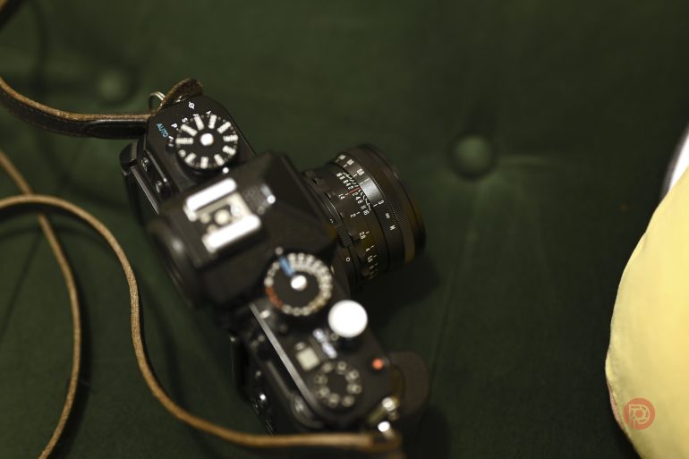 A close-up of a black camera with a lens and strap, placed on a dark green cushioned surface.
