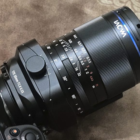 A Nikon camera with a mounted Laowa lens placed on a patterned brown surface.