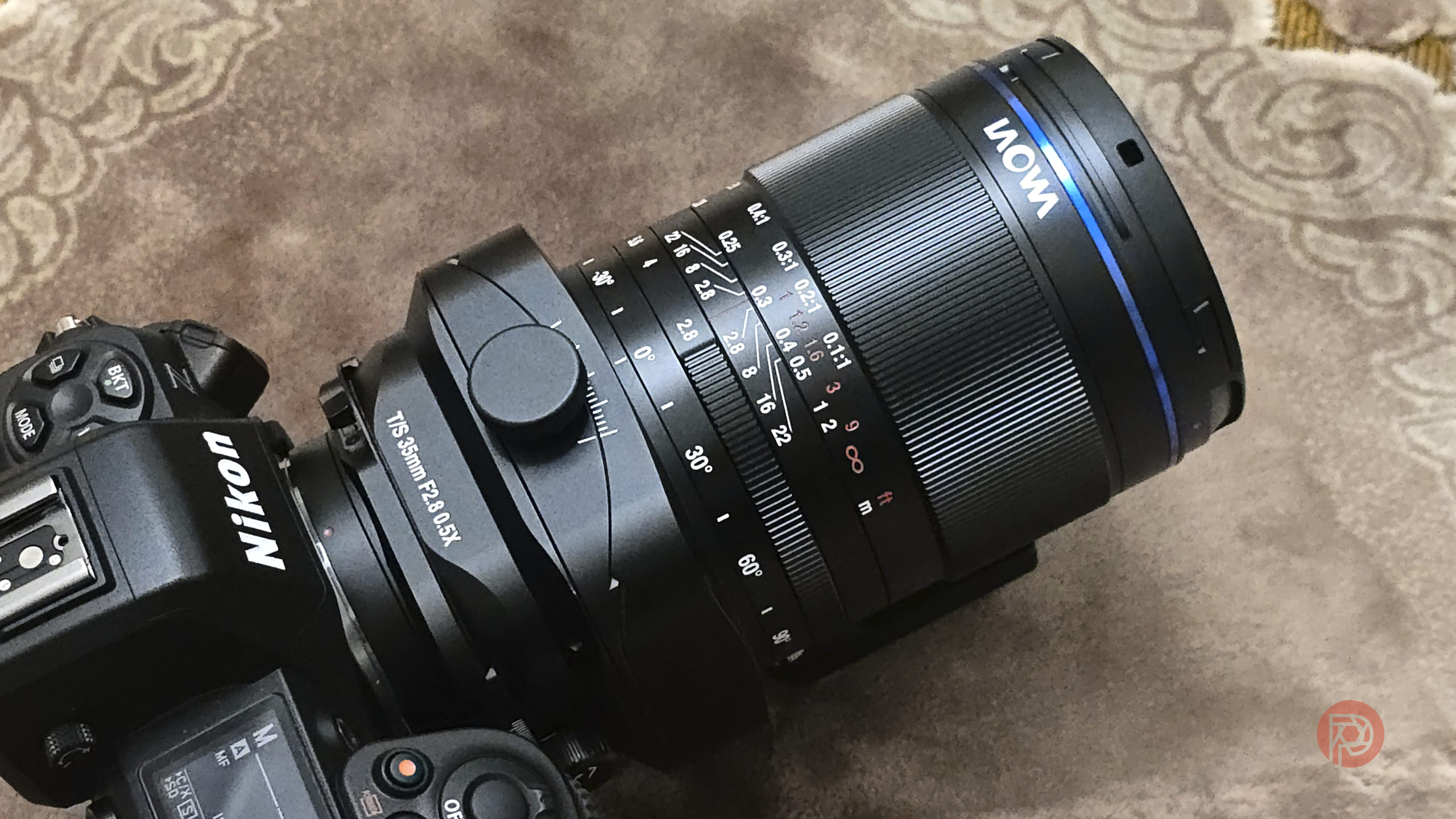 A Nikon camera with a mounted Laowa lens placed on a patterned brown surface.
