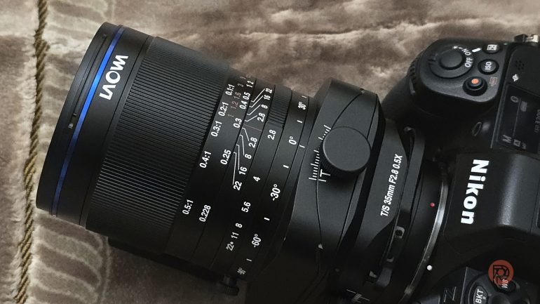 Close-up of a Nikon camera with a Laowa 75mm f/2.8 lens, resting on a soft, beige surface.