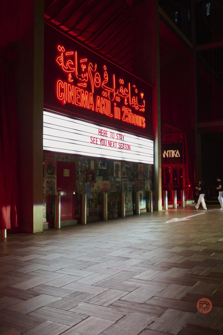 Cinema Akil entrance with neon red sign and marquee reading HERE TO STAY, SEE YOU NEXT SEASON at night.
