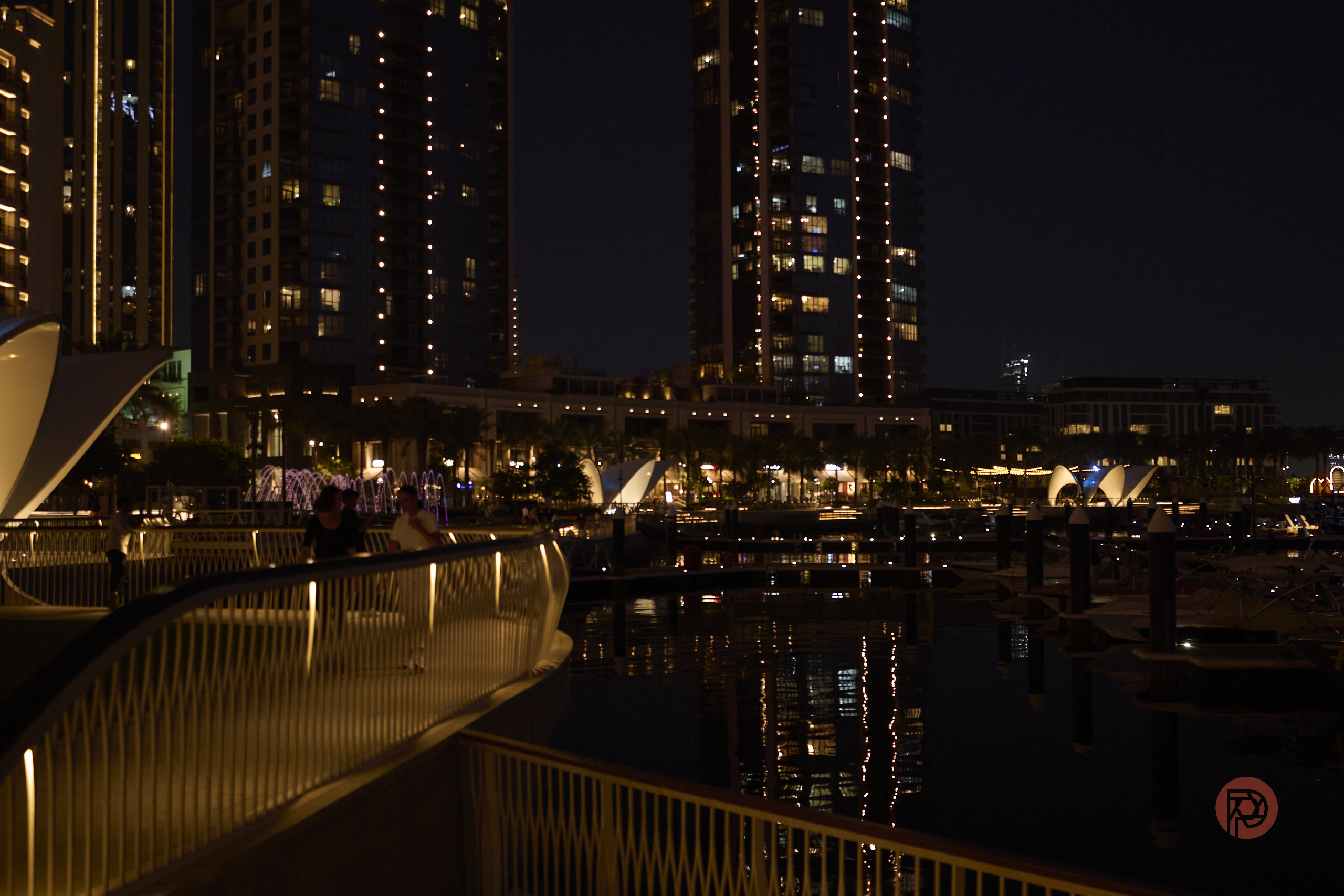 Opinion: Adding AI to Tilt Shift Could Really Change Things Modern city buildings and waterfront at night, with lights reflecting on the water and illuminated walkways.