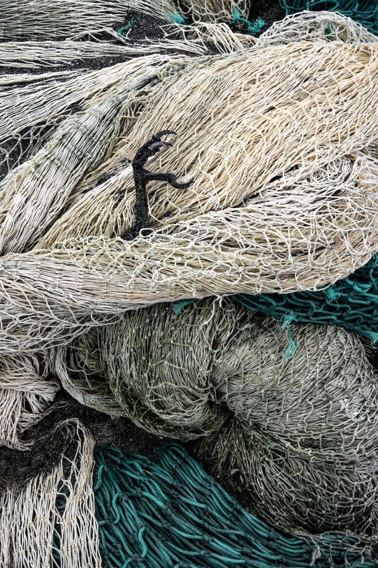 A close-up of tangled fishing nets in beige, green, and black colors.