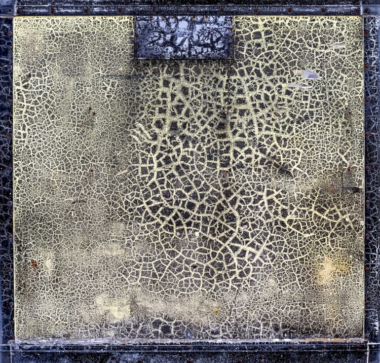 A square panel with a cracked, yellowish surface surrounded by a dark, weathered border.