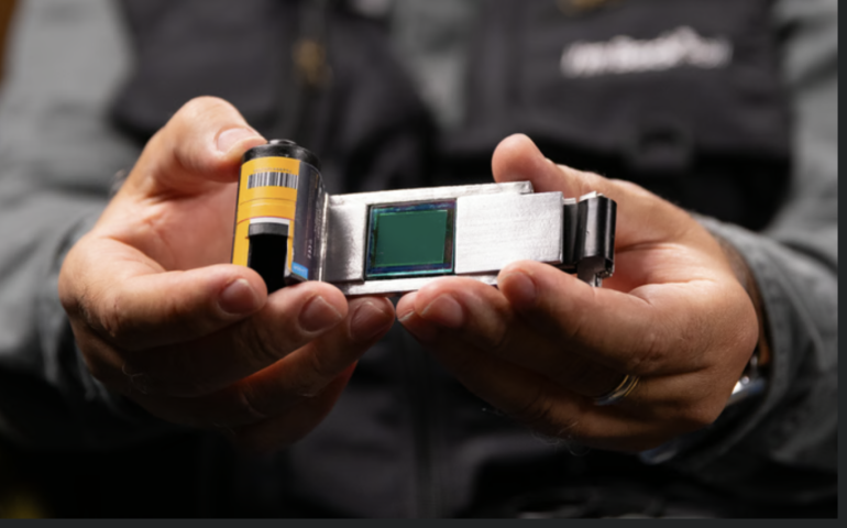 Close-up of hands holding a film canister and a digital camera sensor side by side for comparison.