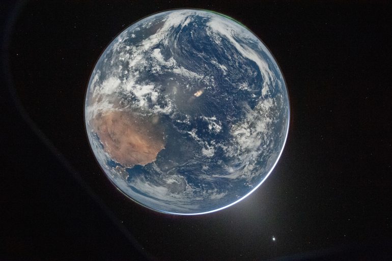 View of Earth from space showing clouds, oceans, and land with a star visible in the dark background.