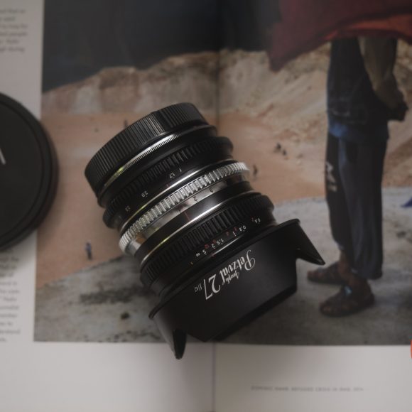 Close-up of a camera lens and lens cap resting on an open magazine with a photo of a person outdoors.