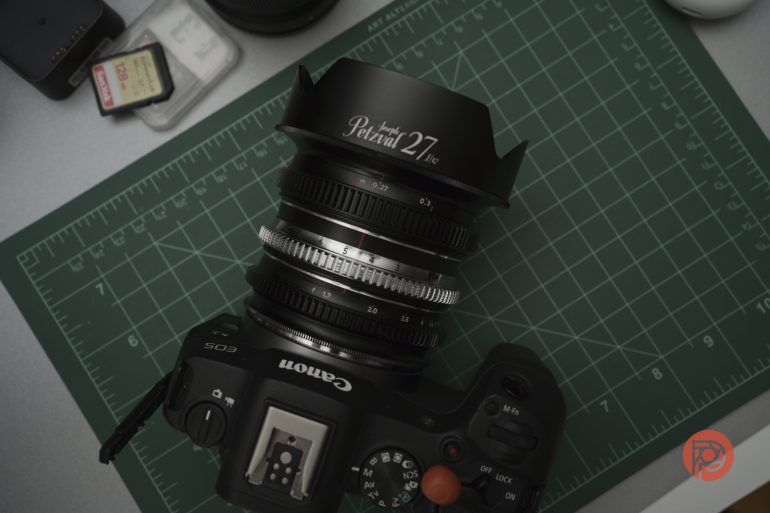 Canon EOS camera with a Petzval 27 lens on a green cutting mat, with SD cards and small electronics nearby.