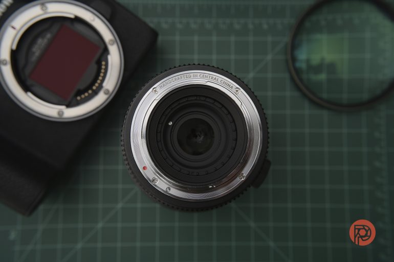 A camera lens viewed from above, placed on a green cutting mat with a camera body and lens filter nearby.