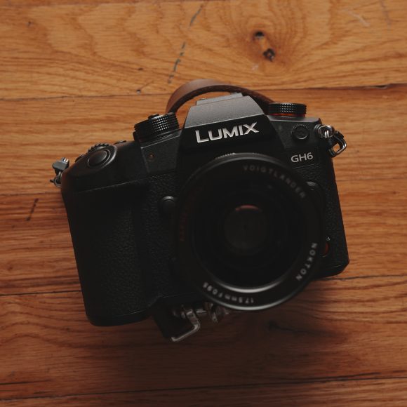 A black Lumix GH6 camera rests on a wooden surface, viewed from above.