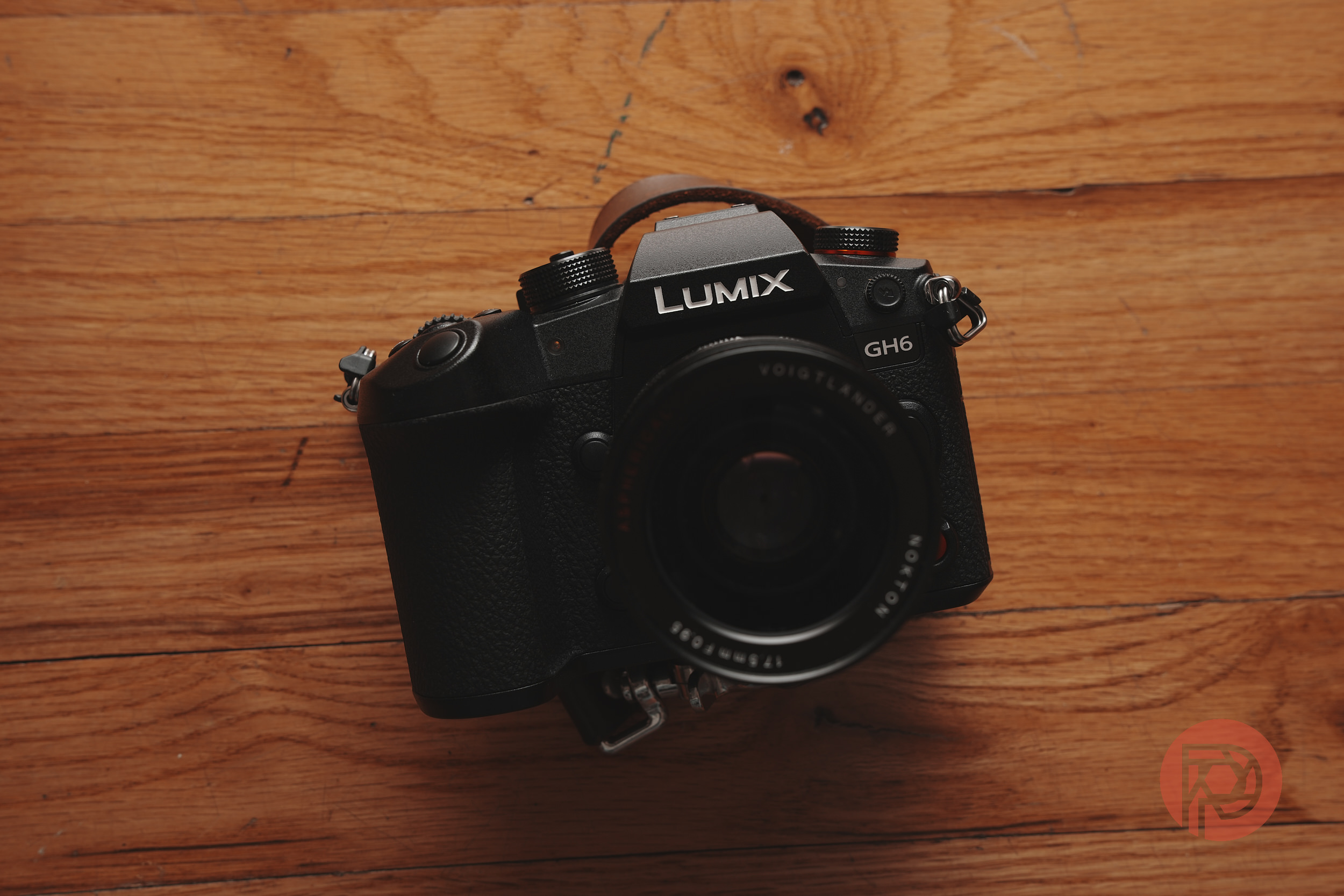 A black Lumix GH6 camera rests on a wooden surface, viewed from above.