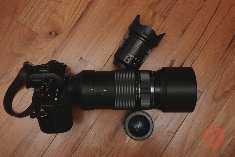 A camera with a large telephoto lens and two smaller camera lenses on a wooden floor.