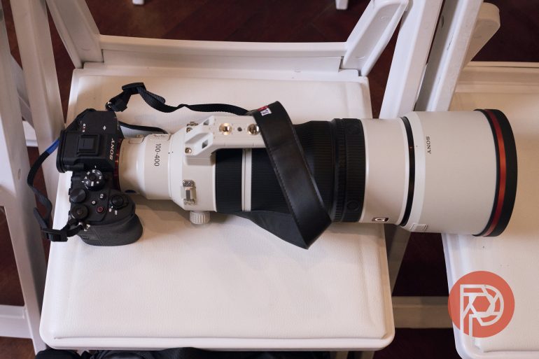A Sony camera with a large telephoto lens rests on a white chair indoors.