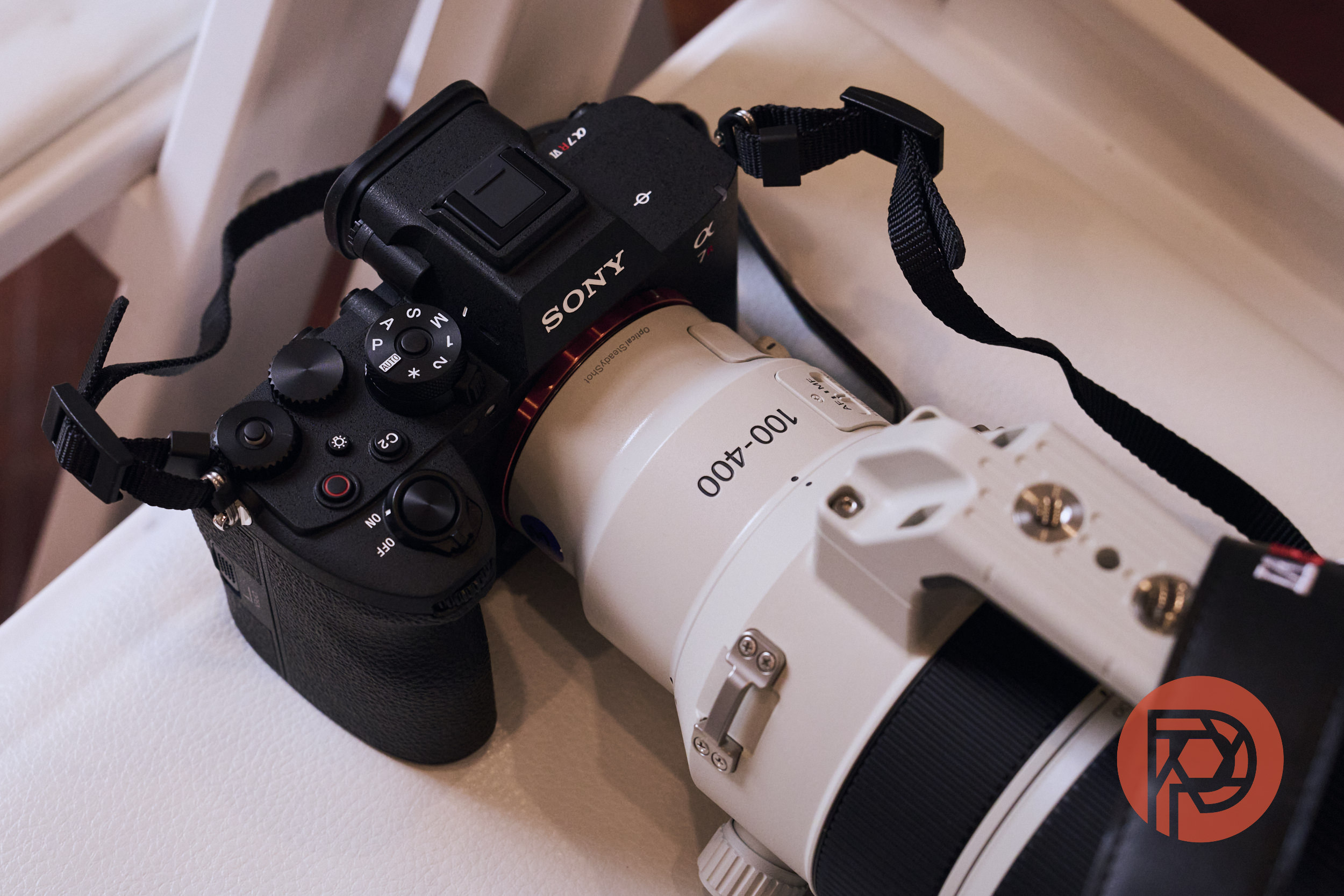 A Sony camera with a white 100-400mm lens rests on a white surface.