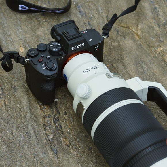A Sony Alpha camera with a large white 100-400mm lens rests on a textured stone surface.