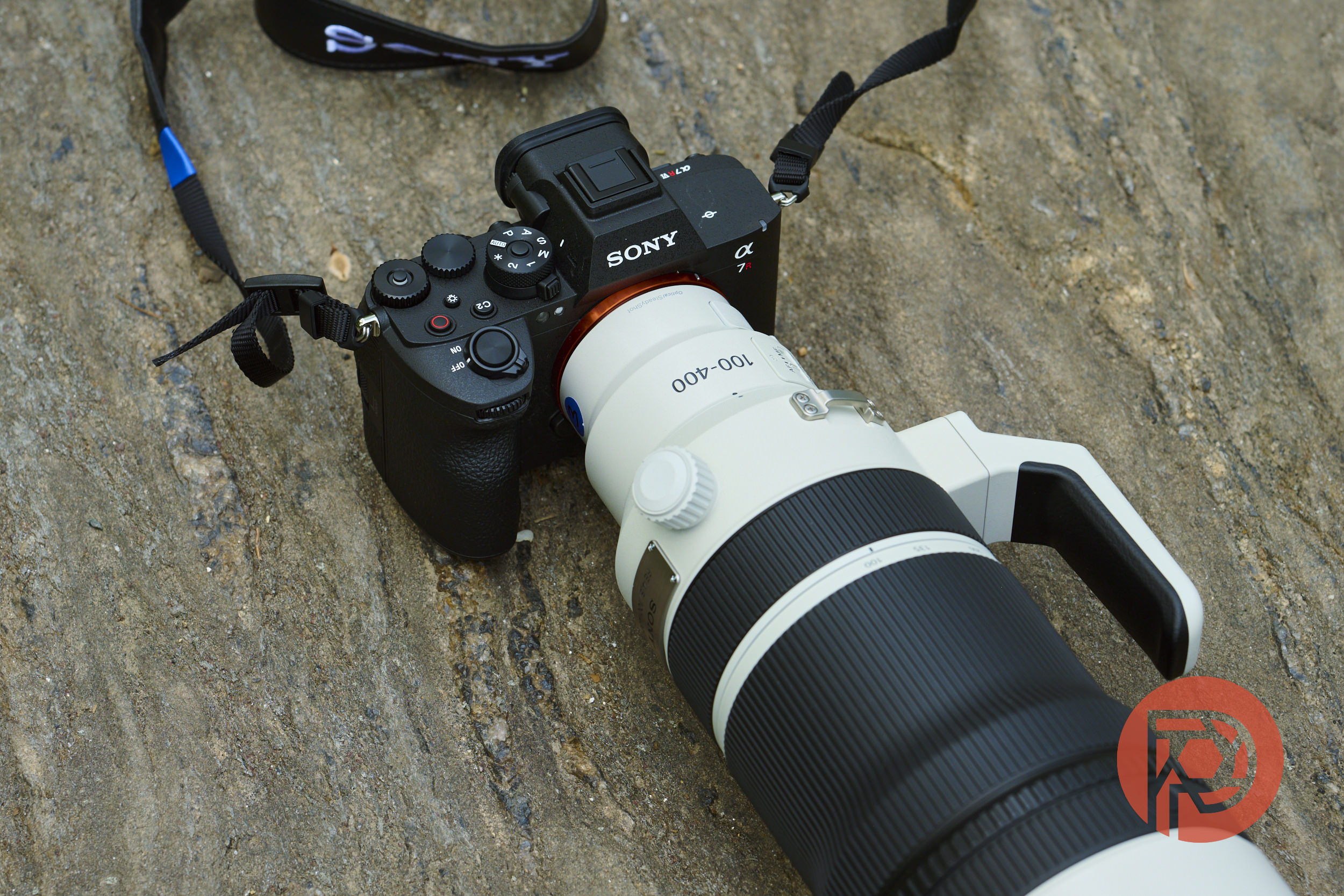 A Sony Alpha camera with a large white 100-400mm lens rests on a textured stone surface.