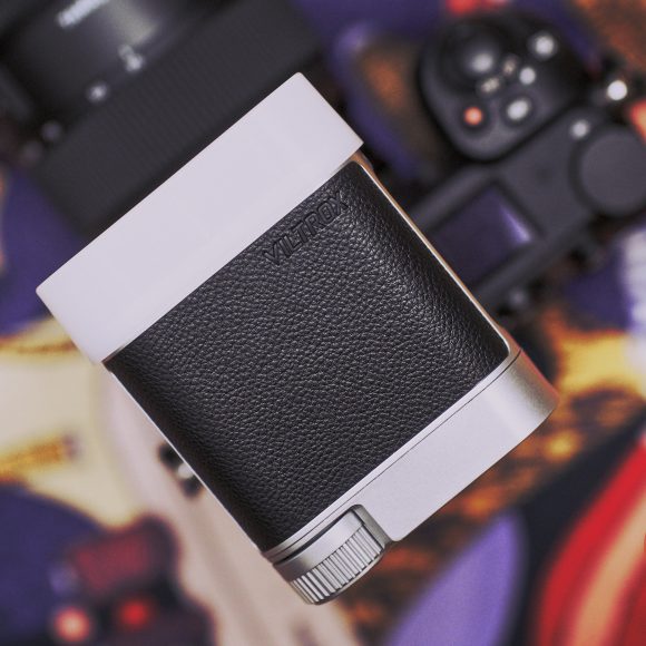 Close-up of a camera with a textured grip and lens, placed on a colorful, blurred background.