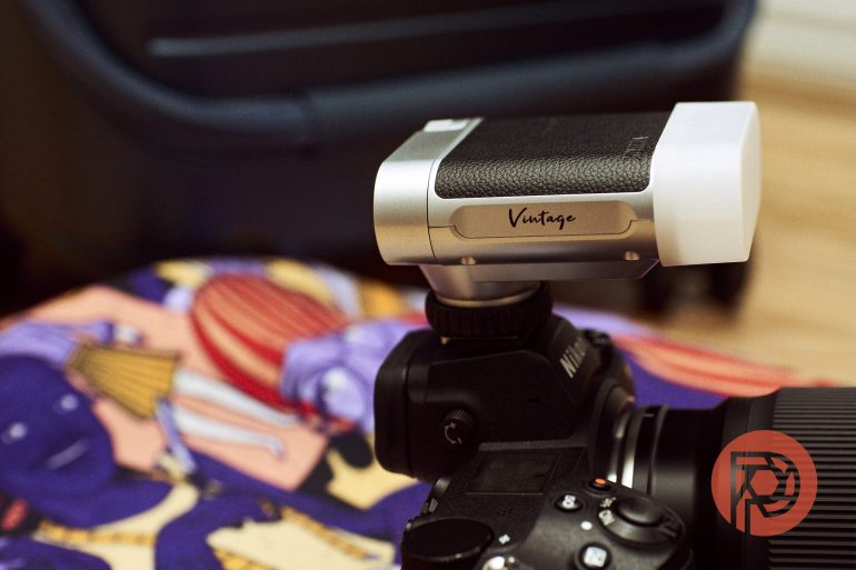 A digital camera with a Vintage flash attachment, resting on a colorful patterned fabric.