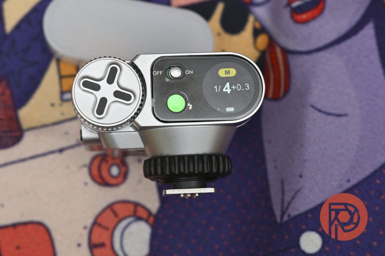 A close-up of a digital camera light meter on a colorful illustrated fabric background.