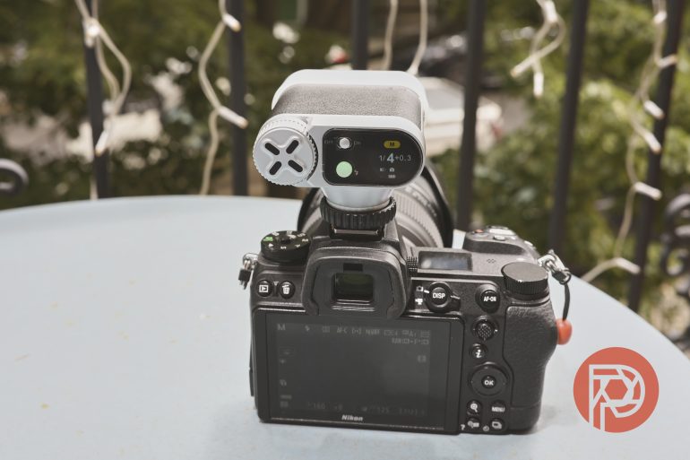 A Nikon camera with a light meter attached, sitting on a blue table outdoors.