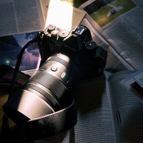A Nikon camera with a zoom lens rests on open magazines under a beam of light.
