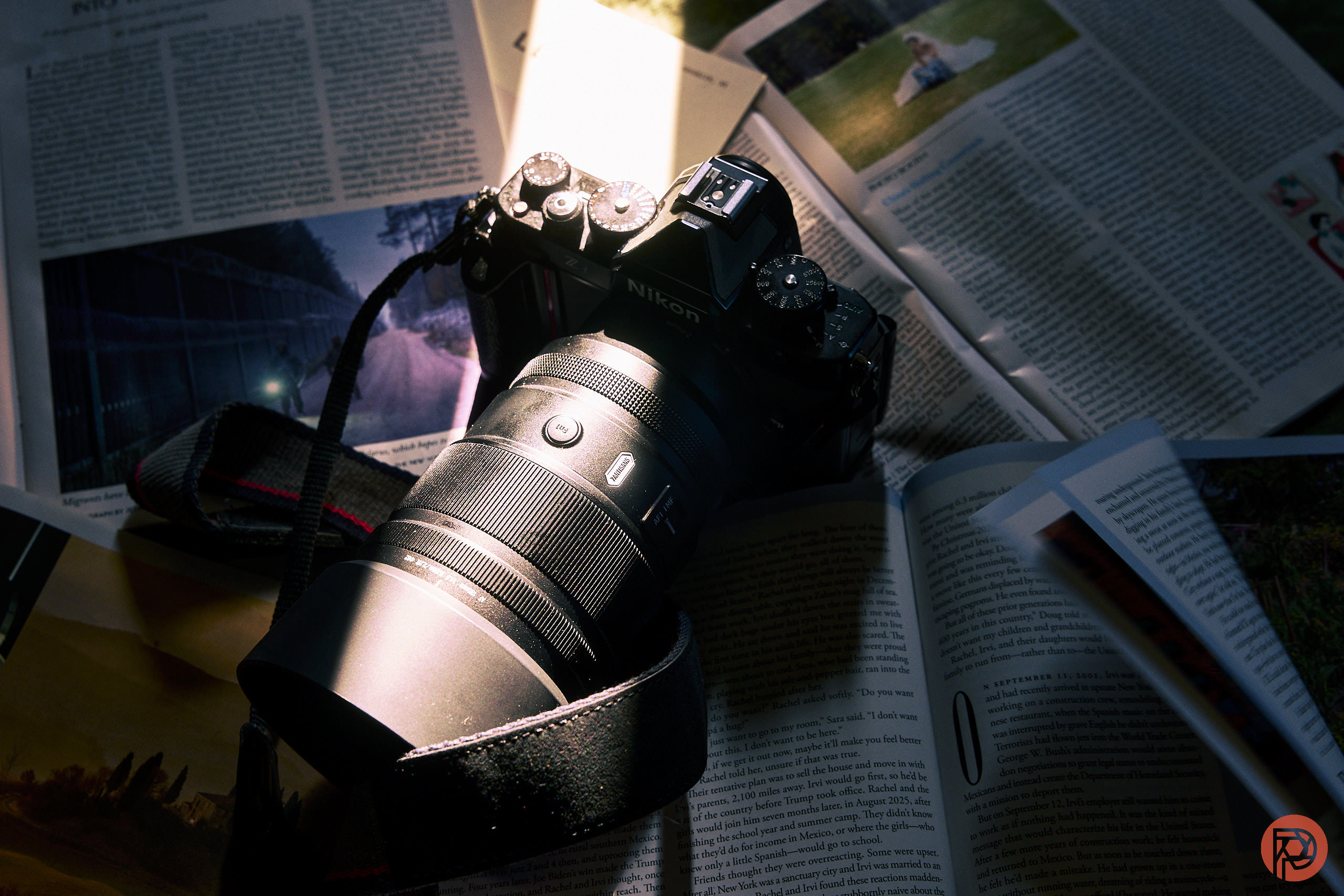 A Nikon camera with a zoom lens rests on open magazines under a beam of light.