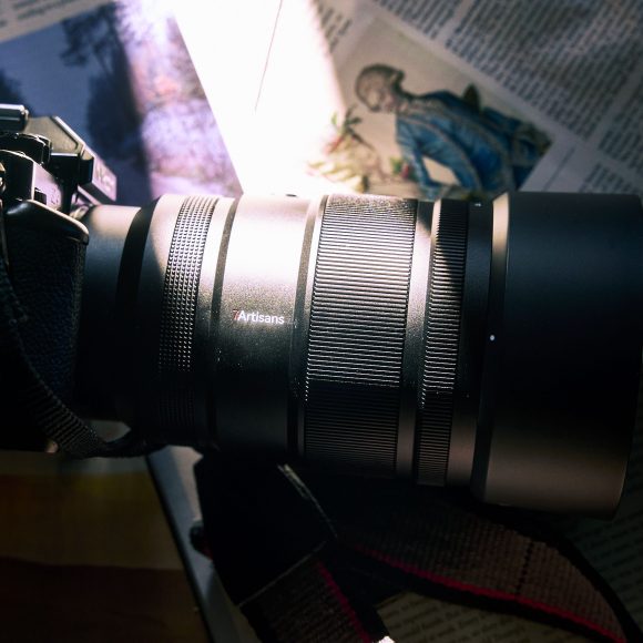 A black camera with a large lens resting on open magazines in sunlight.