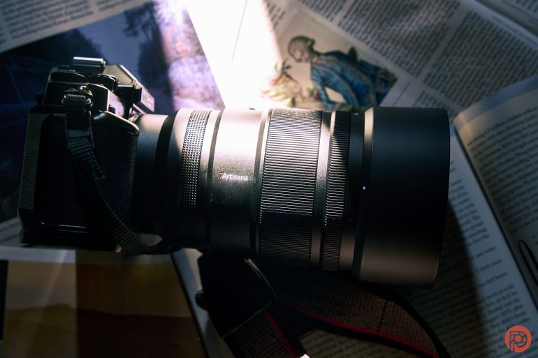 A black camera with a large lens resting on open magazines in sunlight.